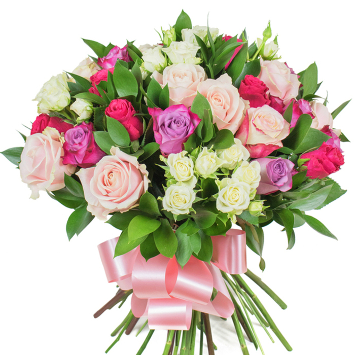 A richly composed bouquet of mixed roses photographed against a stark white background, where colour and texture are the focus. The arrangement is dense and rounded, dominated by generous, open roses in delicate pastel pink and creamy white that reveal soft, ruffled petal edges; vibrant magenta-pink (deep fuchsia) roses provide bold, joyful accents, while a smattering of lavender-hued roses introduces a subtle, romantic coolness. Small spray roses in creamy-white with hints of pale yellow are tucked into cavities between the larger flowers, creating visual pockets of fine detail and gentle contrast in size and form. Interwoven among the blooms are abundant dark green, glossy leaves - probably ruscus or salal - whose elongated, lustrous surfaces offer a polished counterpoint to the matte softness of the petals. The gathered stems below are substantial, showing green and brown tones, and are neatly secured by a broad, baby-pink satin ribbon tied into an elegant, voluminous bow whose tails drape beneath the bouquet and catch reflected highlights. Imagine the scent as a soft, classic rose perfume, tempered by fresh, green undertones, conjuring a quiet spring morning near Clerkenwell Green or along Rosebery Avenue. The mood is celebratory yet refined - a floral composition suited to anniversaries, Valentine's gestures, or a heartfelt birthday present - crafted with the attentive hand of a neighbourhood florist who values balance, colour harmony, and lasting freshness.
