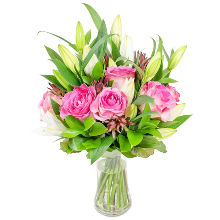 Against a bright white backdrop, a gracefully rounded bouquet is displayed in a transparent, slightly tapered glass vase that makes the blooms feel weightless and fresh. At its centre are several large pink roses, petals unfurling in layered waves of fuchsia and soft blush, their surfaces satiny and full-bodied. Sprung among the roses are tall white lily buds, many still closed with pale green tips, while a few trumpet-shaped flowers have begun to reveal their inner folds, lending a vertical contrast to the roundness of the roses. The arrangement is generously built up with varied greenery - broader, pointed leaves that give structure, alongside smaller, glossy leaflets and feathery sprigs that soften the edges and add movement. Small, darker reddish-brown buds or accent foliage are discreetly dotted through the stems, introducing texture and a shadowed counterpoint to the luminous petals. Clear water in the vase shows neatly cut stems, emphasising the bouquet's freshly prepared quality and the precision of the florist's hand. This composition evokes the calm sophistication of Clerkenwell life - the kind of bouquet that would sit beautifully on a table by Leather Lane or as a hostess gift delivered after an evening at Smithfield - suitable for anniversaries, Mother's Day, or simply to lift a living room with colour and scent. The overall effect is one of considered beauty: tactile, fragrant, and thoughtfully balanced.