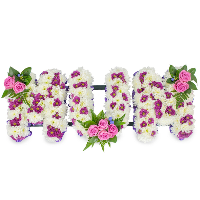 An intimate, three-dimensional memorial spells MUM in generous capital letters, arranged against a clean white background so every contour is visible. Each letter is composed of a dense bed of pristine white chrysanthemums whose soft, clustered petals form a plush, tactile surface reminiscent of fresh snow. Subtle clusters of magenta and purple spray chrysanthemums are interspersed through the white base, creating delicate patterned areas that add shadow and depth to each letter. Three arrangements of vivid pink spray roses serve as focal accents: a small, elegant cluster at the upper left of the left-hand M, a larger, fuller bouquet tucked into the lower curve of the U, and a mirrored grouping at the upper right of the right-hand M. Each rose cluster is accompanied by rich dark green foliage, including slender fern fronds that bring contrast and graceful lines, and by tiny blue accent flowers that flash cool colour like a memory. A slender, dark horizontal bar keeps the letters unified, while a narrow purple ribbon outlines the form and adds a dignified punctuation to the design. The scent is faint and comforting - a green, rose-sweet whisper - and the overall impression is one of respectful craftsmanship, meant to convey lasting love and remembrance. Crafted by Clerkenwell Flowers with an eye for traditional sympathy design, this piece would sit quietly and beautifully at a funeral near Smithfield Market or a memorial service in St John's Square, offering families a personalised expression of grief and honour.