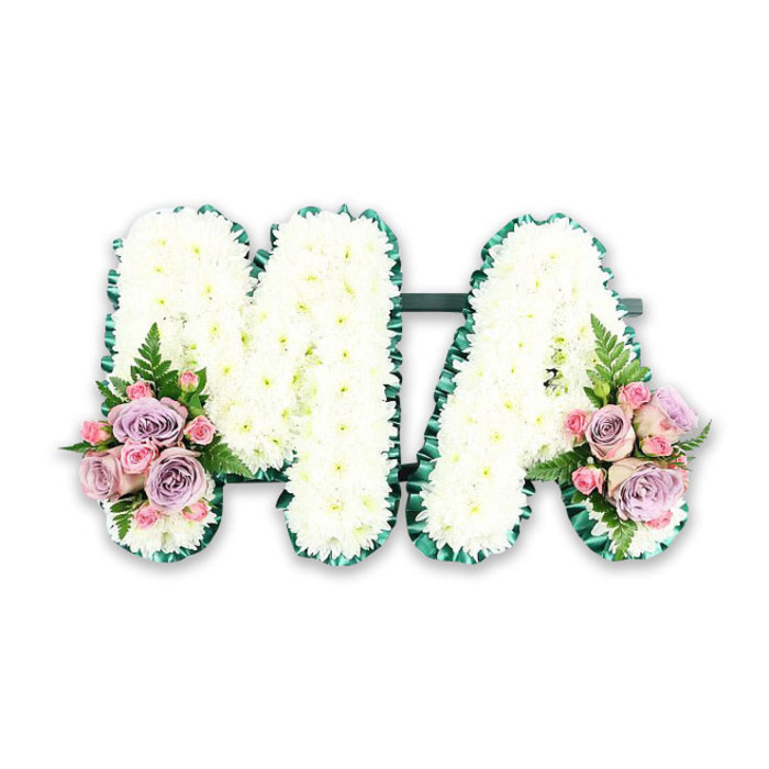 This image shows a carefully constructed funeral flower tribute spelling MA in bold, uppercase letters, designed with the thoughtful precision often seen in bespoke pieces created for families around Clerkenwell. Both letters are built on a sturdy frame and completely covered with pristine white chrysanthemums, each bloom tightly nestled against the next. The petals form a dense, cushiony surface that looks almost like a soft quilt of blossoms, catching the light subtly and giving the tribute a pure, luminous quality. The edges of the M and the A are sharply defined by a band of deep emerald satin ribbon, folded and ruffled into even pleats that trace every angle and curve. This structured green border brings contrast and refinement, just as clean architectural lines stand out along Clerkenwell's mix of historic and modern buildings. A slim horizontal bar of dark foliage visually links the two letters at the base, helping them read as one unified design. At the base of the left leg of the M and the right leg of the A, matching floral clusters soften the strong white shapes. These posies feature a blend of soft lavender roses and pale pink roses, each bloom with delicately layered petals, interspersed with smaller, more tightly budded pink spray roses. A single feather-light fern frond extends from each cluster, introducing a gentle arc of greenery and a feeling of natural movement. Presented crisply against a plain white background, the arrangement appears ready for delivery to a local chapel of rest or home in Clerkenwell, where it would sit beside the coffin or hearse. The tribute's balance of traditional white sympathy flowers and tender pastel accents clearly suggests love for a mother, mama, or Ma, offering a quiet expression of peace, devotion, and lasting memory.
