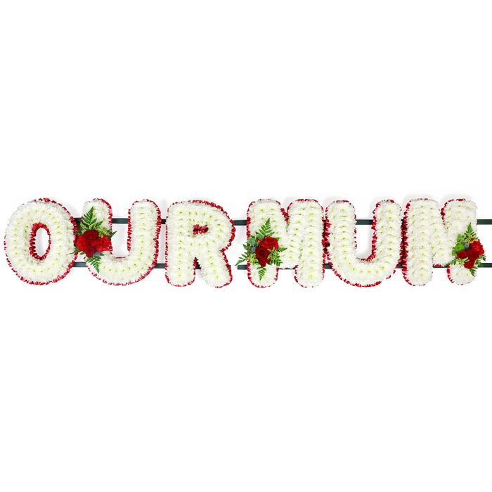 In this image, a carefully constructed OUR MUM funeral flower tribute stretches in a straight line across a clean white background, making each letter and petal easy to imagine. The letters are bold and substantial, filled with compact white chrysanthemum-style florets placed side by side until no gaps remain, creating a soft yet structured cushion effect. The surface of each letter appears gently domed, giving the tribute a three-dimensional presence that suggests it could rest gracefully atop a coffin or be displayed on stands at a service in Clerkenwell. Surrounding the white base, a continuous edging of deep red flowers runs neatly around each letter, their ruffled petals creating a fine, detailed border. This red frame gives clarity to the shapes of the O, U, R, and the two Ms, allowing the message to be read easily even from a distance in a large chapel or crematorium. Subtle dark green support bars link the letters from behind, almost disappearing into the design but ensuring the tribute is strong enough for safe delivery and display. Adding a personal and romantic note, three distinct clusters of red roses with fresh green foliage are nestled into the arrangement. One sits harmoniously between the O and U, another between the U and first M, and the final cluster rests close to the outer edge of the second M. The roses, with their rich colour and velvety petals, express deep affection and respect, echoing the quiet love shared in many family homes around Clerkenwell. Overall, the tribute feels calm, dignified, and deeply personal, a fitting floral farewell for a much-loved mum.