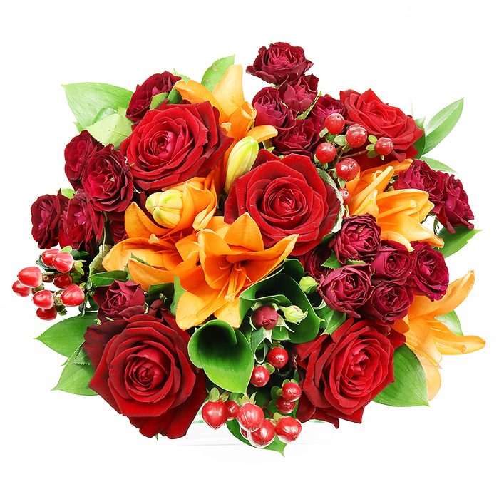 Captured from directly above on a clean white ground, this abundant bouquet is a circular celebration of red, orange and green that reads as both joyful and refined. At its heart several deep red roses bloom fully, their velvety petals opened wide to reveal complex, layered centres that convey classic passion and softness to the touch. Interwoven among them are bright orange Asiatic lilies, their trumpet-shaped petals sometimes dotted with subtle specks and often showing prominent stamens-some blooms opened in full theatrical pose, others held in tight, promising buds for a staggered reveal. Small, dark burgundy spray roses cluster throughout, their compact, multi-headed forms adding luxurious texture and a richer tonal depth beneath the larger flowers. Glossy, round hypericum berries-ruby red and reflective-are sprinkled through the composition like tiny ornaments, catching the light and offering a crisp textural contrast to the petals' sueded surfaces. Broad, glossy leaves of ruscus or salal peek from between blooms, their cool green tones framing the warm palette and lending structure to the arrangement. The lighting is gentle and uniform, emphasising surfaces and contours while preserving the bouquet's saturated colours against the white background; it feels as though the arrangement has been laid out on a studio table near Clerkenwell Green, close to Leather Lane market, for final inspection. The imagined scent is layered: a bright, citrus-spicy whisper from the lilies balanced by the deep, enveloping perfume of roses. Hand-tied with an eye for balance and depth, this bouquet suits anniversaries, romantic gestures, or a dramatic autumn centrepiece, and can be prepared locally by Clerkenwell Flowers for delivery around Spa Fields and Farringdon.