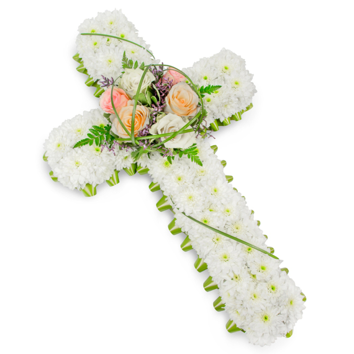 This image shows an elegant floral cross, designed as a classic funeral tribute, resting against a bright white backdrop so that every detail of the workmanship is clearly visible. The cross itself is entirely covered with small white chrysanthemums, meticulously placed so there are no gaps, creating a seamless, plush surface. The texture is soft and inviting, resembling a blanket of tiny, full-petalled stars all pressed gently together. Running around the perimeter of the cross is a slim, vivid green border of foliage, crisply outlining the shape and giving it a polished, professional finish. The contrast between the cool white petals and the fresh green frame suggests both calm and renewal, in the same way the planted beds and trees around nearby Spa Fields bring a touch of nature to Clerkenwell's streets. At the centre where the arms of the cross meet, a raised spray of roses forms the emotional heart of the piece. These roses bloom in warm shades of peach, coral-blush, and creamy ivory, their colours subtly blending into one another. Nestled among them are sprays of light, airy fern, narrow arcs of bright green grass, and little flecks of purple filler flowers that lend a fine-textured, almost lace-like detail. The overall mood is one of reverent beauty: not ostentatious, but quietly confident and deeply respectful. This floral cross would feel at home at a church service, crematorium chapel, or graveside ceremony in and around Clerkenwell, expressing love, faith, and remembrance in a way that feels both traditional and gently personal, like a final, carefully chosen gift for someone dearly missed.