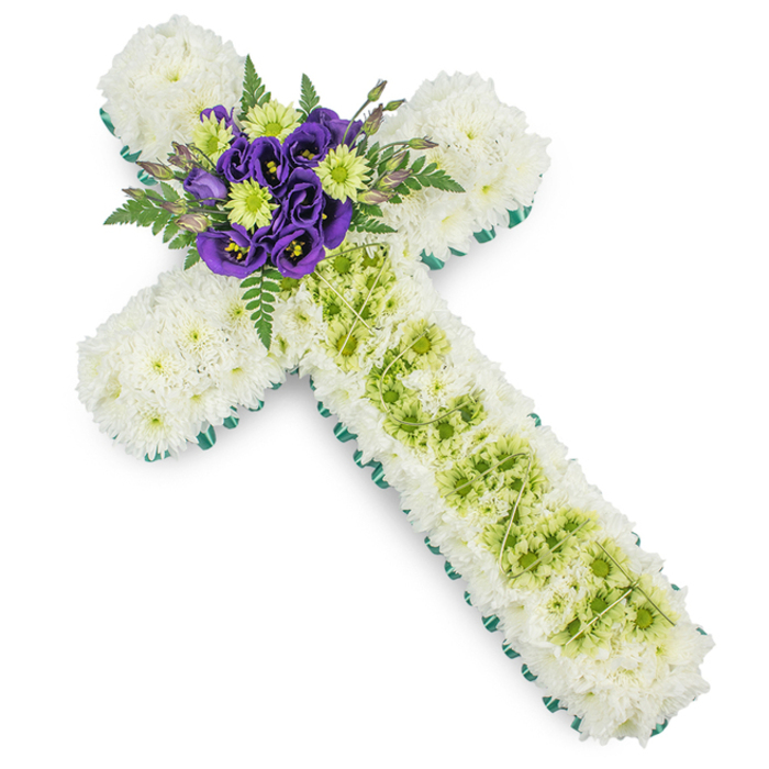 The image presents a dignified floral cross, crafted as a funeral or memorial tribute by a skilled local florist serving the Clerkenwell area. Set against a plain white background, the cross is fully cushioned with small white spray chrysanthemums, their petals forming a dense, plush layer that reads as calm and comforting from a distance. Each stem has been placed so closely that there are no gaps, creating the impression of a soft, snowy blanket shaped into the familiar Christian symbol of faith. A narrow, vivid green border of ribbon or foliage traces the entire perimeter, sharpening the outline and giving the design a fresh, contemporary edge that still feels respectful and traditional. Down the centre of the long vertical arm, a contrasting panel of lime-green button chrysanthemums runs from just below the focal point towards the base, adding a gentle brightness that suggests renewal and the promise of spring. Fine decorative wires, pale green or silvery in tone, are carefully draped in a criss-cross pattern across this central panel, adding a subtle geometric detail that enhances the texture without competing with the flowers. At the junction where the arms meet, a compact spray of deep purple lisianthus provides a natural focal point; their velvety petals, layered and slightly ruffled, are interspersed with bright lime-green button blooms that echo the central panel. Dark green fern fronds and leafy foliage fan out behind and around this cluster, adding depth, movement, and a touch of woodland softness. The overall effect is one of quiet elegance and heartfelt reverence, a floral cross arrangement suitable for services in Clerkenwell churches or local crematoria, where families gather to say a final, tender goodbye.