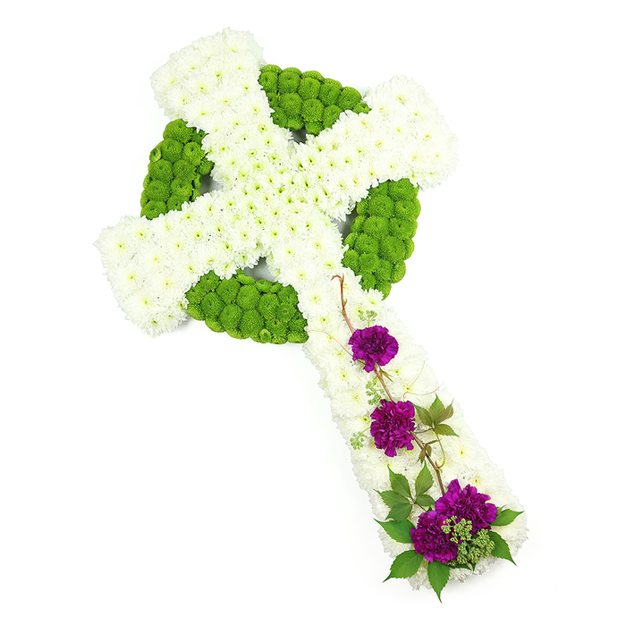 A striking Celtic cross funeral tribute is laid out diagonally from the top-left to the bottom-right of a spotless white background, its form sharply defined yet softened by layers of delicate petals. The cross is composed almost entirely of chrysanthemums, arranged with the precision of an experienced Clerkenwell florist. At its core, the vertical stem and horizontal bar are packed with countless small, white chrysanthemum blooms, tightly clustered so that their petals merge into a continuous, cloud-like surface. Surrounding these white panels, and forming the iconic circle that links the cross arms, run bands of lime green button chrysanthemums. Their compact, round flower heads form a crisp border and fill the inner shapes of the Celtic motif, giving the piece a sense of depth and gently sculpted relief. The interplay of white and green evokes purity and renewal, often requested by local families arranging services near Smithfield or Sadler's Wells who wish to balance tradition with a modern, fresh look. On the lower part of the vertical arm, three distinct sprays of deep purple carnations are grouped with care, each cluster slightly different in size but harmoniously placed. Their richly coloured, ruffled petals bring a note of solemn beauty and quiet affection. Woven through and around these carnations are slender trails of dark green foliage, perhaps ivy or a similar climber, which arc and curl naturally, softening the geometric lines of the cross. The lighting is bright and even, revealing every nuance of petal and leaf, so that the tribute appears alive with texture yet calm in spirit. Overall, this Celtic cross design feels deeply respectful, a meaningful sympathy arrangement for honouring a loved one's heritage and faith within the Clerkenwell community.