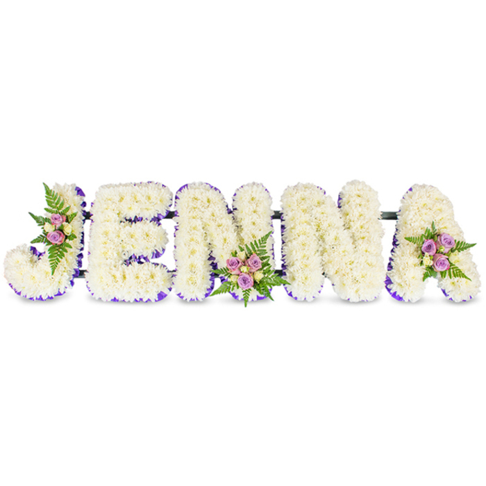 Lovingly arranged for a memorial or funeral, this bespoke floral tribute spells JENNA in strong, three-dimensional letters, each carefully formed from a tight blanket of creamy-white chrysanthemums or similar small blooms that create a soft, cloud-like texture when viewed up close. The letters are outlined on their inner edges with a rich purple trim-either a narrow satin ribbon or a delicate line of tiny lavender blossoms-that lends contrast and sculptural definition to the otherwise immaculate white composition. Three artful clusters of accent flowers add quiet warmth: the J carries a sweep of blush-pink spray roses mixed with pale cream buds tucked into its upper curve; the first N shows a compact cluster of lavender-tinted sprays and soft yellow-cream roses at its base; and the A is finished with a gentle grouping of pale-lilac roses and fern fronds at its top. The roses' velvety petals and the ferns' delicate, feathered foliage introduce texture and a subtle fragrance that soften the formality of the lettered tribute. Thin, dark connecting bars run discreetly behind the letters, keeping the display cohesive and sturdy for placement on an easel or stand in a chapel or funeral reception. As Clerkenwell Flowers would arrange for families in Clerkenwell, Farringdon and the surrounding streets, the piece balances professional craftsmanship with tender intent-an elegant, personal way to express sympathy, remembrance and the quiet beauty of a life celebrated.