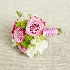 Laid carefully on a pale, natural linen-style cloth, this delicate bouquet appears as if it has been paused between photos on a wedding morning somewhere off St John Street in Clerkenwell. Three open pink roses take centre stage, their petals spiralling outward in layers that deepen from a soft, powder blush at the core to richer, almost raspberry edges at the outermost curls. Around them, plump lime-green button chrysanthemums form lively, rounded tufts, the tiny, tightly packed petals creating a cheerful, almost pom-pom texture that enlivens the arrangement and highlights the roses' satin-like softness. Threaded gently through the bouquet are creamy white filler flowers-likely lisianthus or freesia-with slender buds and cup-shaped blooms that give the design a sense of serenity and space. Smaller starry white blossoms with yellow centres nestle in the gaps, adding delicate points of light and fine detail that suggest careful, experienced hands at work. The stems are hand-tied and trimmed cleanly, wrapped in a vivid fuchsia satin ribbon whose smooth sheen catches the soft, even light. Over this handle, a thin strand of white faux pearls is woven diagonally, like a bracelet wrapped around the bouquet, adding understated glamour suited to bridesmaids or a modern city bride. The neutral, textured background lets the pinks, greens, and whites glow without distraction, creating a feeling of poised anticipation-perfect for wedding photography, bridal party flowers, or intimate celebrations in Clerkenwell loft venues and nearby garden terraces. The bouquet reads as classic yet fresh, crafted with the quiet confidence of a local florist who understands London's contemporary wedding style.