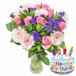 Bathed in gentle morning light, this sumptuous bouquet radiates a quiet, joyful elegance. The composition is a soft interplay of pinks and purples: generous pink Gerbera daisies form open, smiling faces around the arrangement, their pale petals cupped by buttery centres, while flawless pink roses sit slightly higher, their silk-like petals layered with careful restraint to create a feeling of poised romance. Between these principal blooms are tight clusters of vivid purple statice, their crisp, papery texture weaving through the softness of the roses and gerberas to give structure and a lively, three-dimensional rhythm. Glossy deep-green leaves provide a rich backdrop, their sheen catching the light and grounding the palette. The bouquet is gathered and set in a clear glass vase with a modestly widened base so stems and clean water are visible, emphasising the flowers' freshness. A whimsical 'Happy Birthday' motif accompanies the flowers - a small celebratory cake balloon or accent tucked to the side that echoes the bouquet's message of warmth and delight without overwhelming it. The overall scent is faint and sweet, a gentle reminder of garden mornings, and the arrangement reads as a considered birthday gesture from a florist with an eye for balance and sentiment - the sort of floral gift you might carry away from a shop near Clerkenwell Green or delivered to friends working around Farringdon Road.