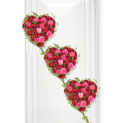 This image presents a graceful trio of heart-shaped funeral tributes, each one composed entirely of red and pink roses and arranged in a gentle diagonal line from the top left to the bottom right, like a flowing ribbon of affection. The hearts are lavishly filled with hundreds of rose heads, their petals overlapping to form a lush, almost quilted texture that feels soft and abundant. Deep crimson roses dominate, carrying the weight of passionate love and profound loss, while scattered among them are bright fuchsia and delicate blush pink roses that introduce notes of tenderness, gratitude, and sweet memory. Around each heart, slender strands of fresh green ivy curve and weave, their small, pointed leaves catching the light and offering a subtle contrast to the rounded rose petals. These ivy trails continue between the hearts, visually stitching them together so they appear connected, as if three chapters of one shared story. The arrangement is photographed against a pure white background, similar to a painted brick or smooth interior wall you might see in a quiet Clerkenwell studio, allowing every colour and contour to stand out with clarity. Soft, even lighting reveals the natural sheen of the petals and the clean edges of each heart, highlighting the precision of the florist's craftsmanship. The overall atmosphere is deeply romantic yet respectful, making this design especially fitting for a farewell that honours a loving partnership, a lifelong marriage, or a cherished family bond, offering comfort and beauty at a difficult time.