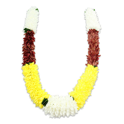 This U-shaped ceremonial mala is presented on a stark white field, the subtle shadow beneath it giving a sense of volume and hand-made presence. From the top of each arm a dense, cylindrical section of creamy white petals-soft and tightly packed like miniature chrysanthemums-draws the eye, then yields to a compact band of deep maroon or reddish-brown that adds solemn depth. A long, plush band of bright yellow follows, composing the generous lower curve and evoking the warmth of marigolds at a celebration. At the meeting point of the curve sits a broad, focal cluster of pure white chrysanthemums, slightly wider than the arms and threaded with small dark green leaf accents that punctuate the colour changes and suggest a measured, traditional rhythm. The flowers are clearly artificial-fine fabric petals layered in thousands to create a durable, tactile surface-but they read with surprising naturalism under the soft light, as if inviting a respectful touch. As an experienced Clerkenwell florist I can picture this piece arriving from our bench near Leather Lane, used for a puja set on a Farringdon windowsill or draped at a wedding entrance; its palette signals purity, prosperity and devotion. The garland's construction and weight suggest careful assembly for ceremonial repetition-an offering that balances visual splendour with practical durability for festivals like Diwali or Holi and for repeated temple use in and around Clerkenwell.