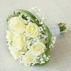 Bathed in gentle natural light, this bouquet radiates a quiet sophistication that mirrors the understated charm of Clerkenwell's leafy streets. White and pale yellow roses nestle together, their petals luminous and almost translucent, catching the day's clarity in ways both serene and inviting. Tiny white stars of baby's breath dance around the roses, their soft texture reminiscent of lace delicately draped along a wedding gown-bringing with them a sense of hope and celebratory promise. Loops of fresh green bear grass weave dynamically through the blooms, offering a modern twist that feels at home in the creative pulse of the neighbourhood. The elegant handle, wrapped in smooth silver satin and adorned with rows of pearlescent beads, beckons a gentle hold-its cool luxury a subtle nod to the area's artisanal craft heritage. Thoughtfully prepared by local florists near St John's Gate, this bouquet is perfect for a special day in Clerkenwell or for marking life's cherished milestones with a heartfelt flourish. Each element, from texture to tone, echoes the beauty and romance cherished by couples celebrating in London's historic heart.