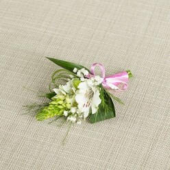 A refined floral boutonniere, carefully composed as if by an experienced Clerkenwell florist preparing for a ceremony off Farringdon Road, lies on a pale, linen-like fabric that has a subtle, natural weave. The neutral, light beige background gives the scene a calm, uncluttered feel, drawing the eye straight to the central white alstroemeria blossom. Its petals are smooth yet slightly ruffled at the edges, opening generously to show a soft ivory centre stippled with fine reddish-brown streaks that cluster near the throat, like delicate handwriting across the flower. Within the bloom, the stamens stand clearly defined, a reminder of its freshness. To the left, a striking spike of vivid green, tightly packed buds-suggestive of Ornithogalum or a similar flower-adds a bold textural accent, each small bud forming part of a sculpted, conical shape that contrasts beautifully with the open, rounded alstroemeria. Sprinkled throughout the arrangement are tiny tufts of white baby's breath, their minute blossoms floating like a light mist, softening the stronger shapes and giving the piece a romantic, airy finish. The foliage underneath is intentionally varied: dark green, sword-shaped leaves create a structured base, while finer, grass-like strands curl and spill outward, echoing a natural, garden-picked feel. At the right edge, the stems are gathered together and wrapped with a narrow satin ribbon in bright pink, tied into a tight, polished bow that brings a joyful pop of colour, ideal for weddings, proms, or anniversary dinners in Clerkenwell's intimate restaurants. The lighting is even and gentle, highlighting the different textures-the velvety petals, glossy leaves, delicate filler flowers, and satiny ribbon-so the entire boutonniere feels fresh, thoughtfully designed, and ready to be pinned to a suit jacket or dress. This image quietly conveys the craft and care behind a small, meaningful floral detail.