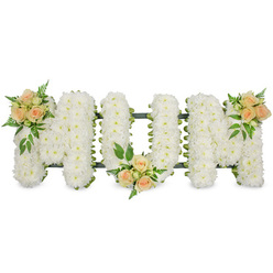 In this carefully composed sympathy tribute, the word "MUM" is shaped from three generous block letters, each one meticulously covered in immaculate white spray chrysanthemums. The flowers are arranged so closely that they form a smooth, cushion-like surface, with the countless tiny petals creating a gentle, rippling texture across the letters. The arrangement sits against a bright, uncluttered white background, which makes every curve and corner of the lettering stand out with clarity. Subtle dark green edging, likely floral ribbon on a sturdy frame, peeks through at the outer contours, giving the piece a crisp outline and steady form. Soft peach and blush pink roses are gathered in three elegant clusters, introducing warmth and tenderness. One cluster crowns the upper left of the first "M," another rests thoughtfully at the base of the central "U," and a final grouping graces the top right of the last "M," forming a calm, rhythmic pattern along the tribute. Each cluster blends open roses, tight buds, and sprigs of lush greenery, including feathery ferns and broader leaves, which lend a natural, garden-fresh feel. The overall impression is one of quiet love and lasting respect, with the pure white chrysanthemums symbolising peace and the rosy accents expressing gratitude and remembrance. It looks like the kind of bespoke funeral arrangement lovingly prepared by a Clerkenwell florist serving local families around Farringdon Road and Spa Fields, designed to lie beside the coffin or on a stand at a crematorium chapel, offering a gentle, dignified goodbye to a cherished mother.
