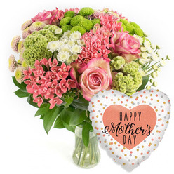 Set against a bright white backdrop, this Mother's Day gift ensemble feels like a moment of calm celebration captured in a studio just off Clerkenwell Road. A rounded bouquet overflows from a clear glass vase, its stems neatly gathered and immersed in clear water, suggesting freshness and careful local preparation. At the centre, full pink roses with softly ruffled petals provide a romantic focal point, their blush tones deepening slightly toward the edges. Around them, tight clusters of coral-pink flowers, similar to kalanchoe, form dense pockets of colour that echo the warmth of a spring morning walk through Spa Fields. Lime-green button chrysanthemums and velvety, frilled green florets bring a lively, modern twist, their vivid hues and textured forms giving the design a playful yet refined character. White daisy-like spray chrysanthemums and tiny multi-petalled blooms with pale pink or yellow-tinted centres add brightness and a gentle airiness, as if light is filtering gently through them. Dark green foliage frames the composition, grounding the pastel and citrus tones with natural depth. Just to the right of the vase, a gleaming heart-shaped foil balloon adds a festive finishing note. Its white or soft silver surface is scattered with irregular gold, silver, and peach polka dots, drawing the eye inward to a bold peach-coloured heart stamped with the words "HAPPY Mother's DAY" in a mix of bold and script black fonts. The image captures the feeling of a carefully curated Mother's Day bouquet and balloon, the kind Clerkenwell Flowers might send for same-day delivery to homes and studios around Farringdon, Barbican, or Sadler's Wells, combining heartfelt sentiment with fresh floral artistry.