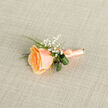 Captured in soft natural light, this compact peach rose boutonniere reads as a portrait of refined simplicity and deliberate care. The central rose blooms with layered petals that melt from a deep golden-apricot core into paler peach tips, each fold suggesting the soft, downy texture of velvet. Tiny clusters of gypsophila punctuate the composition like distant stars, their pristine white dots bringing air and innocence to the arrangement. A small arc of lush green foliage - glossy leaves and a slender fern whisper - adds a fresh, structural contrast that frames the flower and gives the piece a composed silhouette. The stem is finished in a matching peach satin wrap, its gentle sheen and neatly formed knot indicating the handiwork of a practiced hand.

As a florist in Clerkenwell, I picture this pinned on a morning-warm lapel before a walk past Exmouth Market or a quick photograph outside one of the district's restored courtyards; its tones blend beautifully with both formalwear and relaxed city celebration. The scent seems faint but evocative, suggesting orchard blossom rather than overpowering perfume. Crafted with attention to texture, scale and proportion, this boutonniere is ideal for weddings, anniversaries, or intimate gatherings where subtlety matters. At Clerkenwell Flowers we take care to balance visual charm with durability for the day ahead, ensuring pieces arrive fresh and ready to complete a thoughtful look.