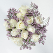 In this overhead photograph, a perfectly rounded bouquet of white roses and lavender limonium sits against a pure white background, creating a feeling of quiet clarity and space. The roses, roughly a dozen in number, are the stars of the design: some remain as neat, promise-filled buds; others are opening into gentle spirals; and several are fully blossomed, their layered centres resembling soft, ivory rosettes. The petals appear thick and velvety, with a satin-like sheen that suggests freshness, as if the bouquet has just been arranged in a Clerkenwell workshop and placed briefly under soft studio light. Surrounding and weaving through the roses, the limonium forms scattered clouds of tiny purple flowers. Each cluster is small and papery, but together they create a misty, ethereal halo that frames the white blooms and gives the arrangement a sense of airiness. The purple hue leans towards a cool, lavender-lilac, echoing the gentle dusk tones you might notice walking past Exmouth Market or along the quieter streets near St James's Church. Only slivers of green stems peek through, keeping the focus firmly on the interplay between white and lavender. The design carries a soothing, contemplative mood, making it especially suited to sympathy occasions where subtle beauty and comfort are desired. It feels like the kind of bouquet chosen to rest beside a framed photograph, accompany a small memorial gathering, or be delivered to a home in Clerkenwell as a soft, reassuring expression of remembrance and support.