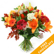 A radiant hand-tied autumn bouquet presented against a crisp white backdrop: open, trumpet-shaped orange lilies take centre stage, their wide petals and dark stamens offering a bold, sculptural focal point, while a few neat lily buds promise further bloom. Nestled around them are happy Gerbera daisies in rich crimson and bright pumpkin orange, their concentric petals creating cheerful, sun-like faces. Soft, ruffled white Lisianthus provide a cool, creamy contrast, their delicate blooms feeling almost silky to the touch. Scattered through the composition are lacy, star-like Astrantia heads with intricate purple-pink centres, introducing a whimsical, architectural texture. Deep green foliage-likely ruscus or salal-forms a lush, glossy base that lifts and frames the flowers, while dramatic, deeply lobed oak leaves in reddish-brown and burnt-orange punctuate the design and reinforce the season's warmth. The stems are gathered in a classic hand-tied style and secured with a dark twine or raffia knot, the cut ends visible below, all arranged under soft, even studio light that highlights petal sheen and leaf veins. The overall impression is one of autumnal abundance: warm, slightly spicy floral scent, layered textures, and a comforting, harvest-time palette that suits a Thanksgiving table, an October birthday, or a cosy house-warming. In the lower right corner a bright orange diagonal banner reads FREE CHOCOLATE in white capitals, an added visual cue of a seasonal offer. The bouquet reads as both carefully composed and delightfully spontaneous-an inviting gift that captures the feel of a crisp Clerkenwell morning near Exmouth Market or the leafy corners of nearby St John's Square.