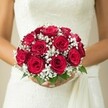 Amid Clerkenwell's storied streets, a bride pauses in the soft daylight, holding an exquisite bouquet that blends timeless elegance with a touch of local artisan flair. Her hands, gracefully manicured, gently cup the base of a perfectly domed bridal bouquet, the vibrant red roses at its core unfurling their thick, velvet petals in a show of deep affection. Each rose, carefully selected for its stage of bloom, speaks to both anticipation and fulfillment-a true mirror of a wedding morning in St John's Square or adjacent parks. With clouds of white gypsophila woven throughout, the bouquet captures an ethereal softness, like a whispered promise carried on Clerkenwell's gentle breezes. Fresh green leaves at the base lend a sense of vitality and connect the design to the lush pockets of greenery scattered across the community. The bride's dress, visible in pristine ivory with hints of lace detail and a flowing fabric sash, adds layers of tactile beauty-its textures quietly shining in the golden, filtered light. The neutral backdrop, softly blurred, ensures every nuance of floral artistry and bridal style shines. Crafted with the expert hands of a local florist attuned to Clerkenwell's unique spirit, this arrangement radiates warmth, hope, and the enduring promise of new beginnings.