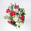 A hand-tied bouquet of red roses, pink-red carnations, soft white daisies, and tiny gypsophila is gathered tightly together, framed by glossy tropical foliage and sprigs of eucalyptus, like a little piece of Clerkenwell's morning light captured in flowers. The image shows velvety crimson rose heads sitting proudly at the centre, their layered petals spiralling outward in rich, romantic tones. Around them, ruffled carnations in vivid pinkish red create a sense of movement, their feathery edges softening the intensity of the roses. Small white daisy-like chrysanthemums with golden centres dot the arrangement, giving a fresh, innocent brightness that lifts the whole palette. Wisps of white gypsophila weave between the larger blooms, creating a cloudlike halo that makes the bouquet feel both airy and full. Eucalyptus stems arc gently from the sides, their cool grey-green leaves adding a modern, almost silvery contrast against the warmer shades. Deep, polished greens at the base provide structure and depth, much like the leafy calm of Spa Fields on a sunny day. The bouquet is shown from above, so the viewer can appreciate the circular balance and careful spacing of each flower, with no stem out of place. The mood is joyful yet composed, perfect for a birthday, a welcome-home gift, or a simple gesture of affection delivered across Clerkenwell's townhouses and studios. You can almost imagine carrying it down St John Street, the subtle fragrance of eucalyptus and rose mingling with the city air, a bright, hopeful bundle of colour cupped in your hands.