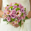 In this photograph, a romantic wedding bouquet is captured as if resting on a windowsill above Clerkenwell's cobbled lanes, bathed in calm daylight. At its centre, dusky mauve and lilac roses unfold in perfect spirals, each bloom full and velvety, their cool tones giving the arrangement a refined, almost poetic charm. Threaded between the roses, loose sprays of baby's breath scatter tiny white blossoms, creating a soft haze that lightens the composition and evokes a whisper of tulle veils and quiet vows. Bright green chrysanthemums, shaped like rounded buttons, punctuate the pastel palette with fresh, springlike energy; their vivid hue suggests the young leaves you might see in St James's Churchyard at the start of the season. Pink alstroemeria arcs gracefully through the design, its slim petals streaked with deeper pink and touches of warm yellow, adding gentle movement and a sense of openness, as though the bouquet is in mid-breath. Glossy foliage gathers everything together, framing the flowers without overwhelming them, and allowing each colour to stand clearly against the next. The stems are trimmed and bound with care, keeping the shape full but airy, ideal for a bride stepping out of a Clerkenwell registry office or converted warehouse venue. Soft highlights along the rose petals and gypsophila suggest freshness and careful conditioning, the kind of detail local florists prize for same-day wedding deliveries across the EC1 area. The bouquet feels both contemporary and timeless, a hand-crafted tribute to love, trust, and shared new beginnings.
