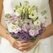 As gentle morning light filters across a Clerkenwell bridal suite, a bouquet of pastel blooms becomes the radiant centrepiece. The bride's hands, nails softly polished in blush pink, cradle a fresh, airy arrangement-a harmony of creamy white lisianthus, cloud-soft pink and lilac stock, and sleek green buds, each chosen with thoughtful care by local artisans. Deep purple starbursts of allium wrap the base in dramatic detail, mirroring the creative vibrancy found in Clerkenwell's gardens and studios. Above, slender loops of dark bear grass enclose the bouquet with grace and structure. Hints of an ivory lace wedding dress shimmer in the blurred background, further highlighting the bouquet's soft hues and elegant textures. Every element-from the fresh, dew-kissed blooms to the intricate foliage-evokes celebration and artistry, perfectly suited for a joyful ceremony on the leafy streets around Farringdon. This bouquet's romantic palette and delicate structure make it a timeless ode to love's gentle beginnings in the heart of London.