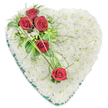 A heart-shaped sympathy tribute is shown in full, resting against a clean white background that allows every flower and detail to stand out clearly. The entire centre of the heart is densely covered with small white chrysanthemums, each bloom placed closely beside the next, forming a thick, cushion-like layer that appears soft yet structured, suggesting comfort and quiet support. Their pure white petals blend into one another, evoking peace and a gentle stillness, much like the quieter side streets off Clerkenwell Road on an early Sunday. Around the outer edge, a wide band of dark green satin ribbon encircles the flowers, giving the heart a defined silhouette and an elegant, finished look. Draped diagonally across the upper left portion of the heart is a graceful spray of five red roses, their deep crimson petals velvety and carefully spiralled. Three roses are grouped prominently at the upper left curve, forming a focal point, while two more extend downward towards the centre, creating a soft diagonal line. Interwoven among the roses are delicate white filler flowers and a mix of greenery, from glossy leaves to fine, feathery sprigs that add lightness and texture. Thin strands of bright green ornamental grass sweep in gentle arcs over the white chrysanthemums, visually linking the roses and giving a sense of movement, as though memories are being traced across the heart. This traditional design would be a thoughtful choice for a funeral or cremation ceremony in Clerkenwell, offering a touching visual expression of love, grief, and enduring connection.