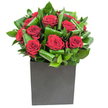 In this elegantly modern arrangement, rich velvety crimson roses form the unmistakable heart of the display, each bloom opening in lush, generous spirals that read like small, satin sculptures. The roses are carefully clustered so their deep red faces press close together, while broad glossy green leaves are looped and curled around them to create a rhythmic frame-each leaf folded with intent to add movement, shine, and a sculptural silhouette. The composition sits low in a matte black cube that gives the bouquet a confident, geometric base; its smooth, flat surface contrasts with the soft petals and the slightly waxy sheen of the foliage, grounding the design with contemporary poise.
Bright, clean lighting picks out highlights on the petals and catches the gleam of water on the inner leaves, lending an almost tactile clarity as if you could run a fingertip along the petals and feel their silken softness. Close to the arrangement there is an airy, fresh green scent layered beneath the classic heady perfume of rose-a subtle, uplifting note that balances the bouquet's romantic intensity. As a florist familiar with Clerkenwell's quiet courtyards and the lively stalls of Exmouth Market, I imagine this piece sitting on a reception desk in a nearby design studio or as the centrepiece for an intimate anniversary dinner on St John's Square.
Crafted with intention, this bouquet reads as both an urban statement and an intimate gesture-perfect for romantic milestones, sincere thanks, or any moment that calls for passionate, refined floristry made for modern London interiors.