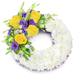 A lovingly crafted funeral wreath formed as a perfect circular 'O', photographed against a plain white backdrop so every detail reads clearly. The main body of the wreath is built from hundreds of small, pristine white spray chrysanthemums packed tightly together to form a plush, cloud-like ring; their multi-layered petals overlap to create a soft, even surface that suggests calm and unity. Nestled on the upper left curve is a single, graceful spray of colour: several fully opened yellow roses in warm butter-to-gold tones, their petals unfurling in gentle spirals, contrasted with clusters of deep royal purple lisianthus (Eustoma), whose ruffled, cup-shaped blooms lend a velvety, dignified presence. A few pale lavender and green lisianthus buds remain closed, adding depth and the sense of natural progression. Interwoven are glossy, rounded leaves, some with subtle variegation, and feathery fern fronds that soften the transition between white and colour while giving the spray structure and movement. A discreet dark purple mesh or crinoline ribbon peeks out beneath the chrysanthemums along both inner and outer edges of the ring, echoing the lisianthus tones and framing the composition. The wreath's open centre reinforces the traditional circular form and the quiet symbolism of continuity and remembrance. In soft, even lighting the textures become tactile: the chrysanthemums feel downy, the roses buttery, and the lisianthus satiny. Intended for a solemn service or as a sympathy tribute, this arrangement reads as an expression of measured warmth and reverence - a handcrafted memorial piece that cradles memory with simplicity and grace, quietly speaking of peace and farewell.