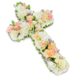 An elegant funeral flower cross rests against a clean white background, its entire shape created from a dense covering of soft, pastel blooms. The cross is instantly recognisable as a Christian symbol, yet its edges are gently rounded by the mass of flowers, giving it a tender, comforting appearance. The main body is built from an abundance of white and ivory roses, their velvety petals opening in precise spirals, interspersed with fluffy clusters of white hydrangea that add a rich, cushion-like texture. Woven through this serene white base are accents of warm colour: peach and apricot roses, pale blush pink roses, and other small pastel blooms that lend warmth and depth without overwhelming the calm palette. Tucked between these are tiny hints of lavender or light purple filler flowers, adding a delicate touch of contrast much like a soft echo of colour in the distance. Small leaves and slender green sprigs peek discreetly from beneath the blossoms, gently defining the outline and ensuring the cross stands out clearly against the background. The lighting is bright but soft, illuminating each petal and casting a slight shadow, which gives the arrangement a sculpted, three-dimensional presence. This is the sort of floral tribute one might see at a memorial or church service in Clerkenwell, perhaps near St James's Church or along Clerkenwell Road, chosen to honour a loved one with a symbol of faith, love and the hope of eternal rest. The overall mood is peaceful, offering quiet comfort to those gathered in farewell.