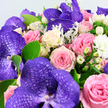 In this photograph, a luxurious floral bouquet completely fills the frame, displaying a harmony of colour and texture that feels perfectly at home in Clerkenwell's creative atmosphere. Large purple Vanda orchids sit proudly across the design, their petals richly saturated and marked with intricate darker violet veining that creates a striking, almost mosaic effect. These exotic blooms are artfully interlaced with a wealth of roses in gentle, romantic tones: powdery blush and soft pink roses just beginning to open, deeper medium pink roses giving warmth and depth, and creamy white and pale yellow roses whose petals are still neatly cupped, signalling exceptional freshness. Dotted among the petals are rounded clusters of white Hypericum berries, their smooth, waxy surfaces providing a crisp, modern texture. Smaller white filler flowers-likely miniature chrysanthemums or petite carnations-peek through like soft clouds, heightening the bouquet's lush, abundant feel. The greenery weaves through and around the flowers: bright, oval-shaped leaves bring a fresh, garden-like energy, while delicate, silvery fronds similar to Dusty Miller add a cool, velvety contrast along the outer edges. The colours-cool purples, layered pinks, gentle creams, and hints of butter-yellow-create a sense of romantic sophistication, reminiscent of flowers chosen for a stylish Clerkenwell loft wedding or a special celebration near Farringdon Road. The arrangement suggests quiet luxury and heartfelt emotion, suitable for anniversaries, milestone birthdays, or elegant thank-you gifts delivered across EC1. You can almost imagine the subtle fragrance of rose and greenery drifting through a sunlit flat, the bouquet acting as both a centrepiece and a tender expression of affection.