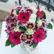 Overflowing with vibrant personality and local charm, this bouquet seems to echo the creative pulse of Clerkenwell. Dominating the rounded arrangement, hot pink Gerberas extend plush petals that catch the ambient daylight, their deep centers drawing the gaze to the heart of the bouquet. Interlaced with precision, clusters of magenta and crisp-white chrysanthemums add playful contrast, each blossom centered on a bold, green disk that radiates freshness. Creamy white roses, unfurling in gentle, upward spirals, lend a touch of time-honored elegance, their soft fragrance hinted at in the subtle play between petals. Wisps of baby's breath float amid the bolder flowers, contributing a breezy, cloud-like texture that lightens the whole design-a nod to Clerkenwell's welcoming squares and open-air cafés. Underneath, lush, glossy foliage provides a rich green base, enhancing each hue and balancing the arrangement's energy. Resting atop a radiant white surface-a kitchen table, perhaps, or a sunlit festival counter-the bouquet is framed by glimpses of ornate railings, evoking Clerkenwell's signature ironwork. A small white tag nestles in the corner, inviting a personal message or heartfelt wish. Perfect for celebrating birthdays, sending thanks, or brightening a local office, this joyful arrangement truly captures the spirit of Clerkenwell living.
